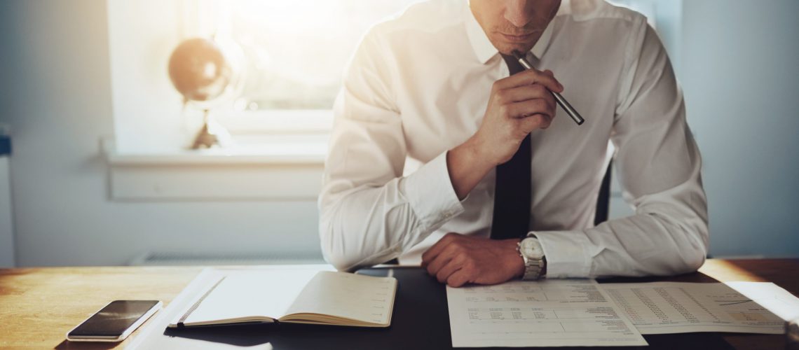 Serious business man working on documents looking concentrated with briefcase and phone on the table