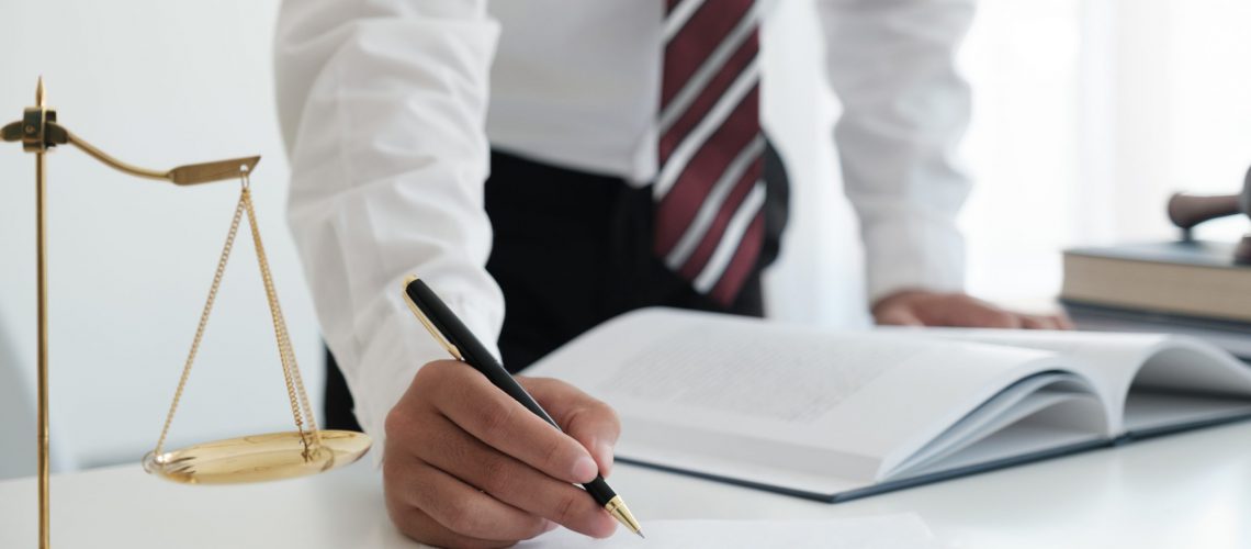 Lawyer sitting working at the desk hand holding pen for signing important documents. lawyer and law ,judiciary and legislature courtroom legal concept.