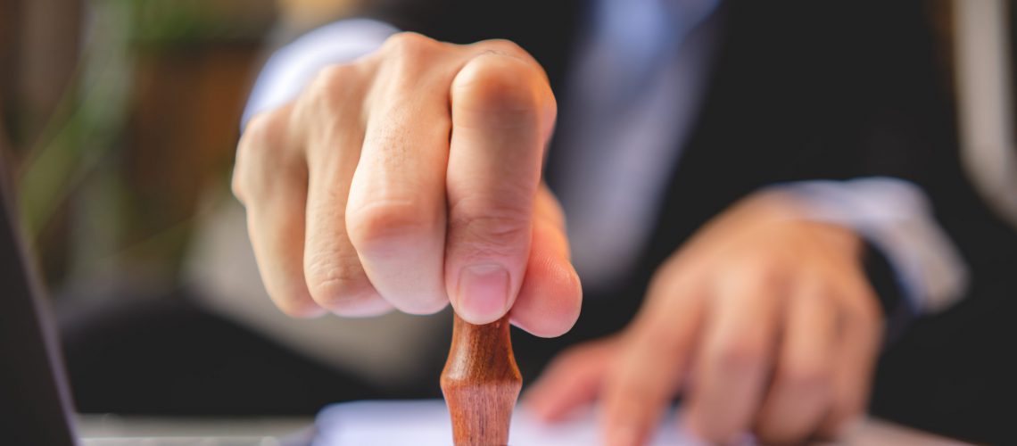 Close-up of a person's hand stamping with approved stamp on approval certificate document public paper at desk, notary or business people work from home, isolated for coronavirus COVID-19 protection